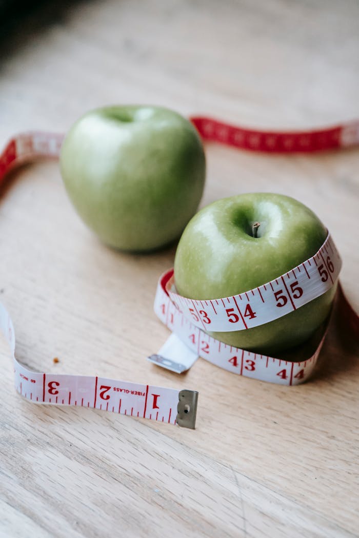 our-services-1 Two green apples on a wooden surface wrapped with a red and white measuring tape, symbolizing health and diet.